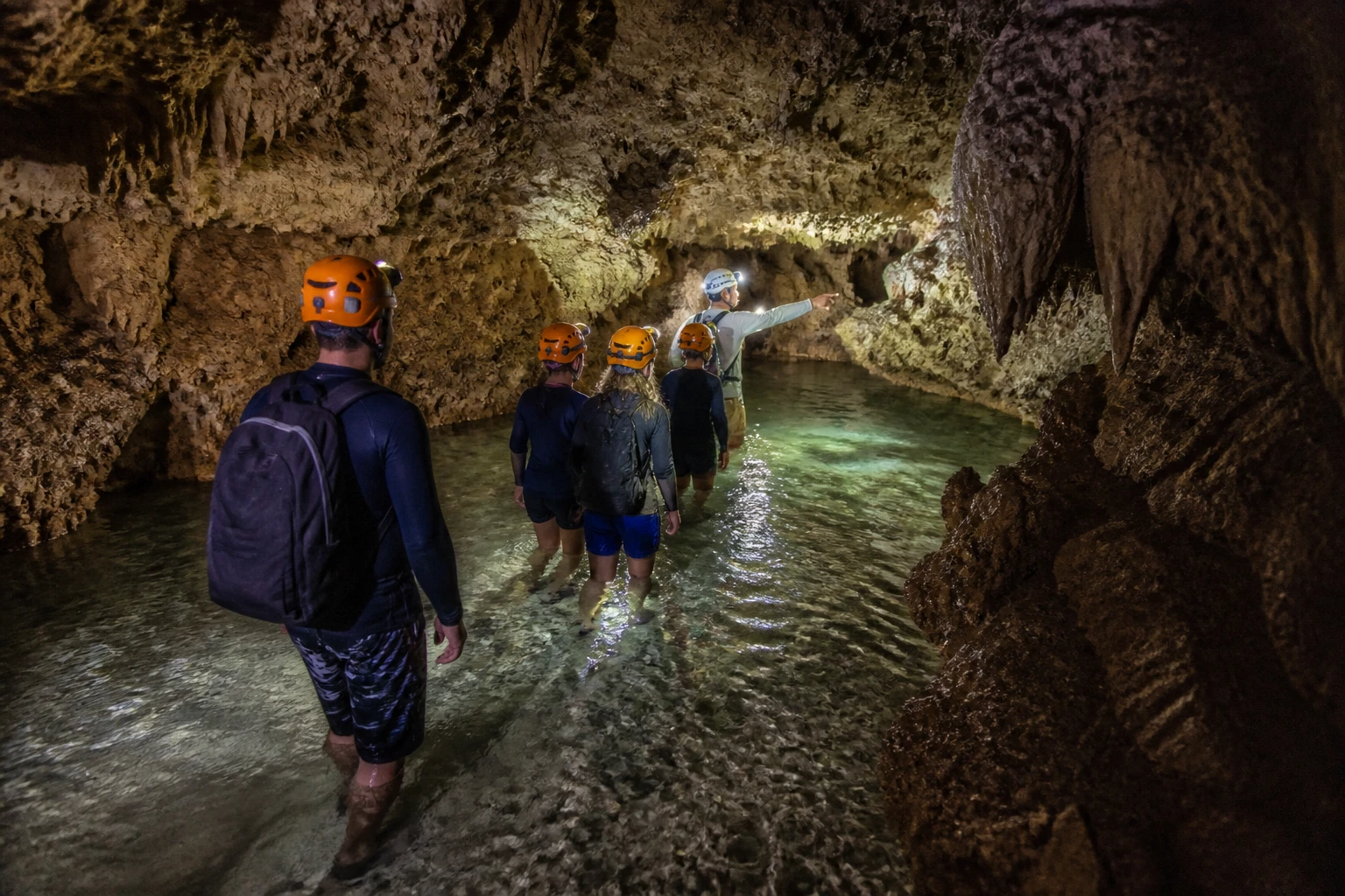 Small guided group moving through shallow cave water with helmet lamps